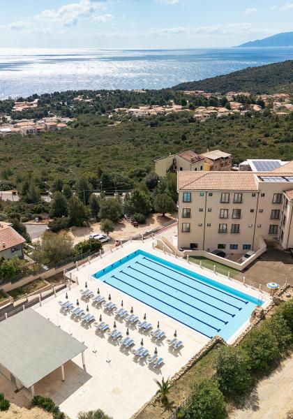 Vue panoramique sur piscine, mer et collines vertes.