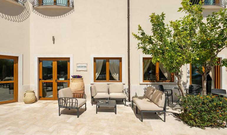 Espace détente extérieur avec chaises, tables, plantes et un panneau 'Réception'.