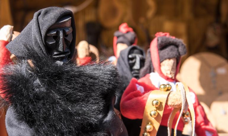 Poupées avec masques traditionnels et vêtements colorés, exposées sur un marché.