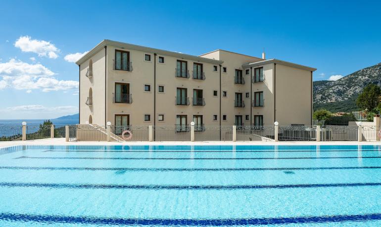 Hotel con piscina e vista mare, cielo sereno.