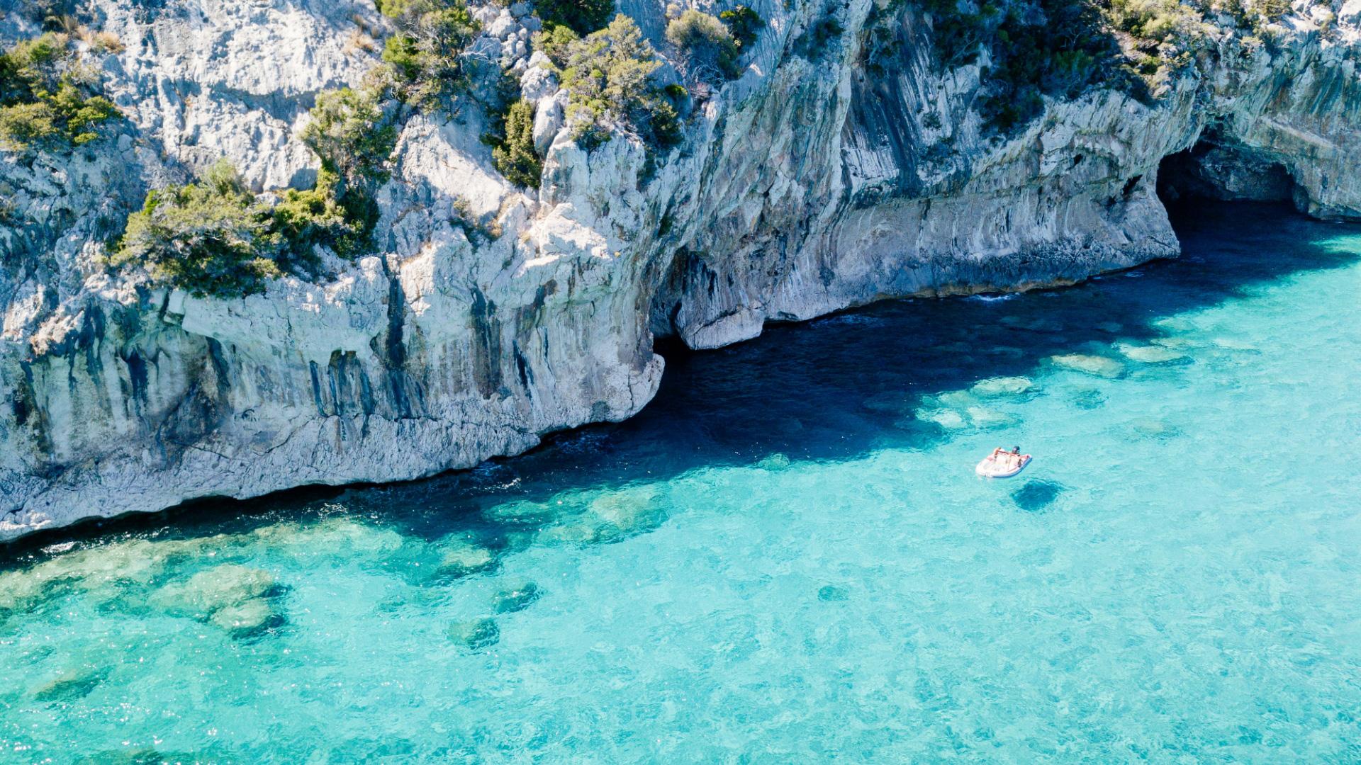 Acque turchesi accarezzano scogliere imponenti, una barca solitaria galleggia serena.