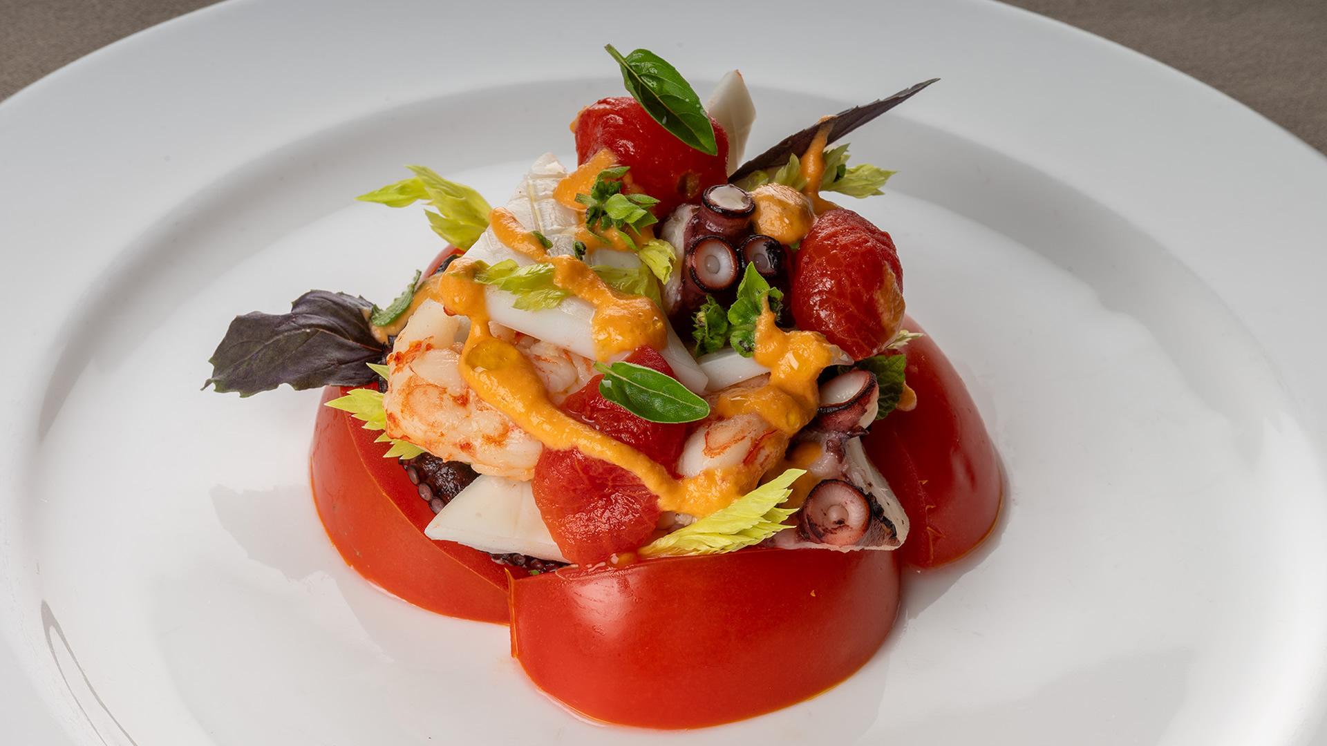 Piatto vibrante di mare con polpo, gamberi e pomodori, ricco di colori e freschezza.
