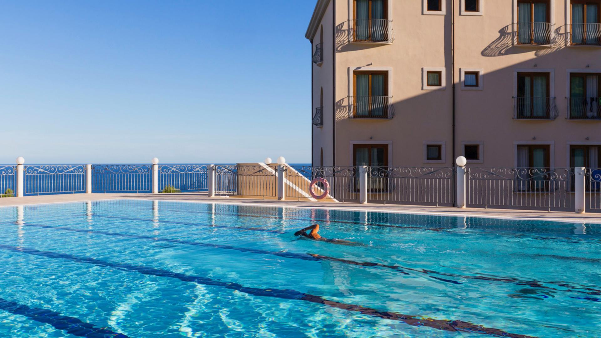 Piscina serena con vista mare e nuotatore solitario, atmosfera di pace e relax.
