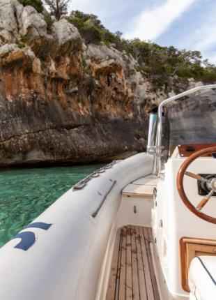 Gommone in acque cristalline, scogliere maestose, natura selvaggia e avventura incombente.